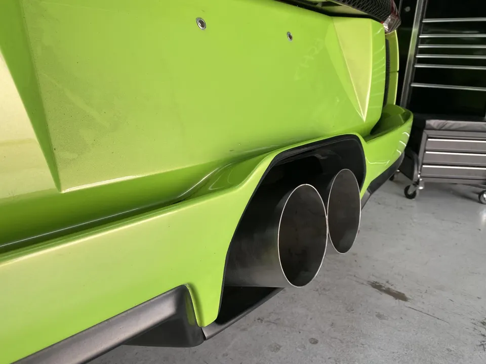 Close-up of the bright green Lamborghini's aftermarket exhaust tips in a shop.