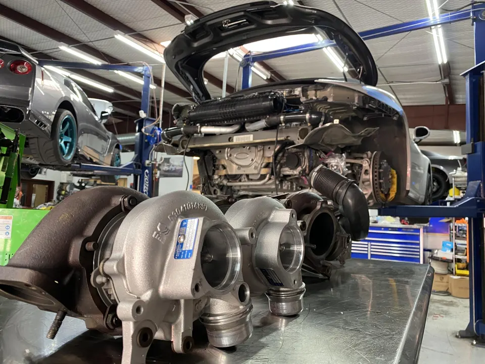 Multiple turbochargers on a workbench in a performance tuning shop with a Porsche and GT-R on lifts.