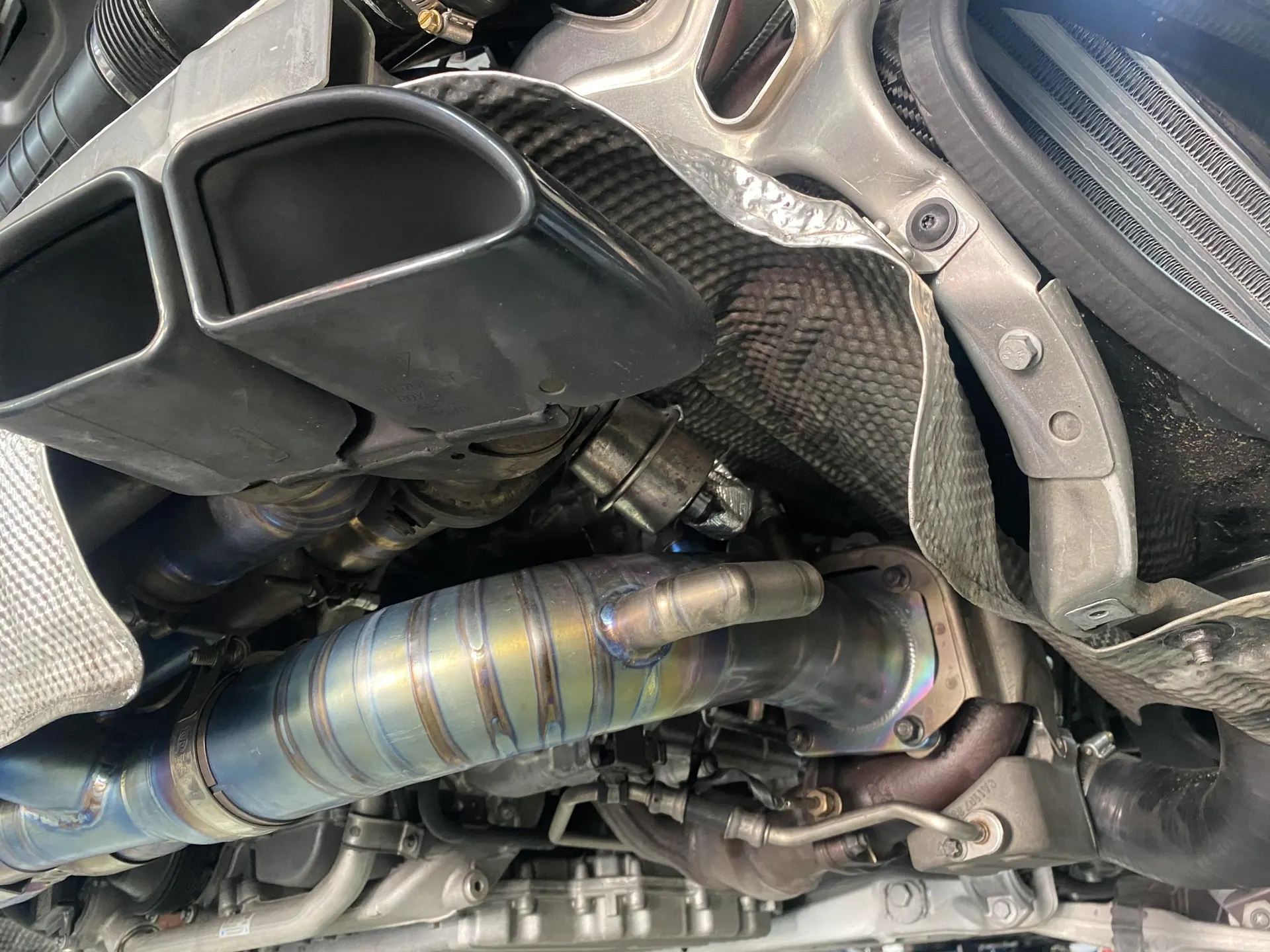Close-up of a car's underside showing an aftermarket titanium exhaust system and black exhaust tips.