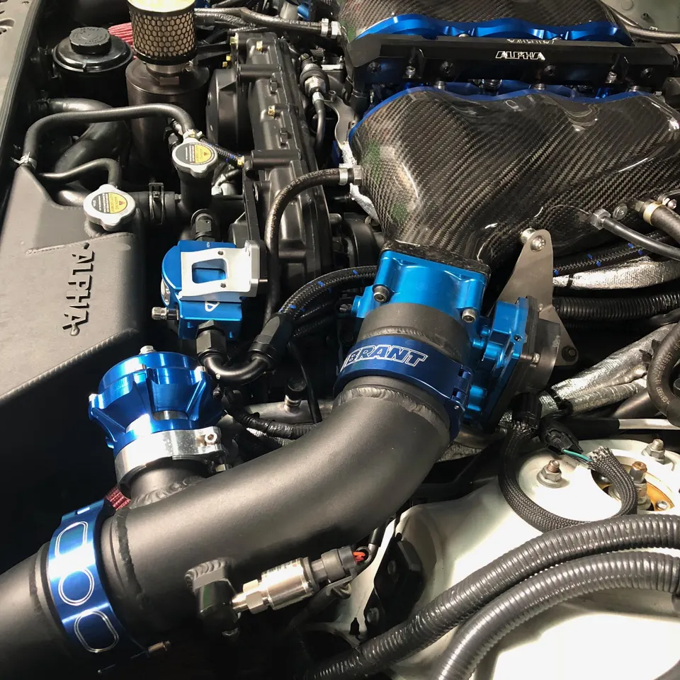 Close-up of a high-performance engine bay featuring a carbon fiber intake manifold, blue throttle body, and blow-off valve.