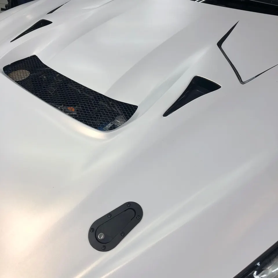 Close-up of a white matte car hood featuring black vents and a black quick-release hood pin.
