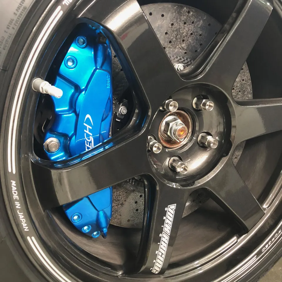 Close-up of a black Volk Racing wheel with a blue Jotech brake caliper and perforated rotor.