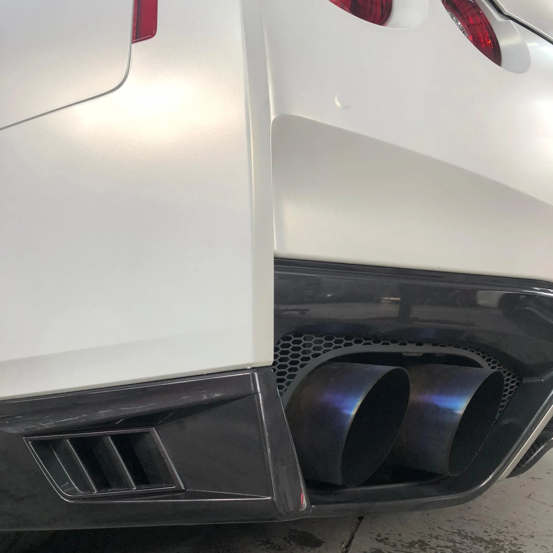 Close-up of a white Nissan GT-R's rear bumper with burnt titanium exhaust tips and a black diffuser.