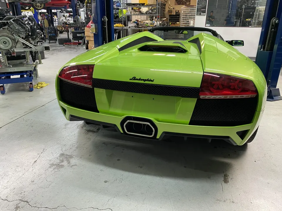 Rear view of a bright green Lamborghini Murcielago Roadster parked in a performance tuning shop.