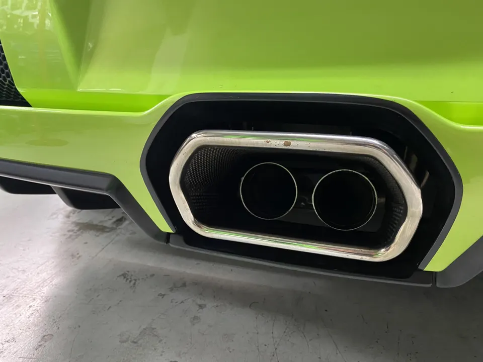 Close-up of a green Lamborghini's dual exhaust tips and rear bumper, showcasing the performance exhaust system.