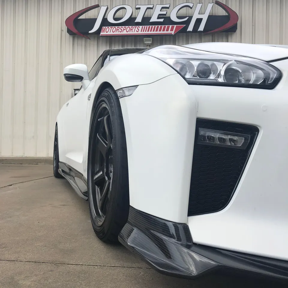 White Nissan GT-R with carbon fiber front splitter and black wheels parked in front of Jotech Motorsports building.