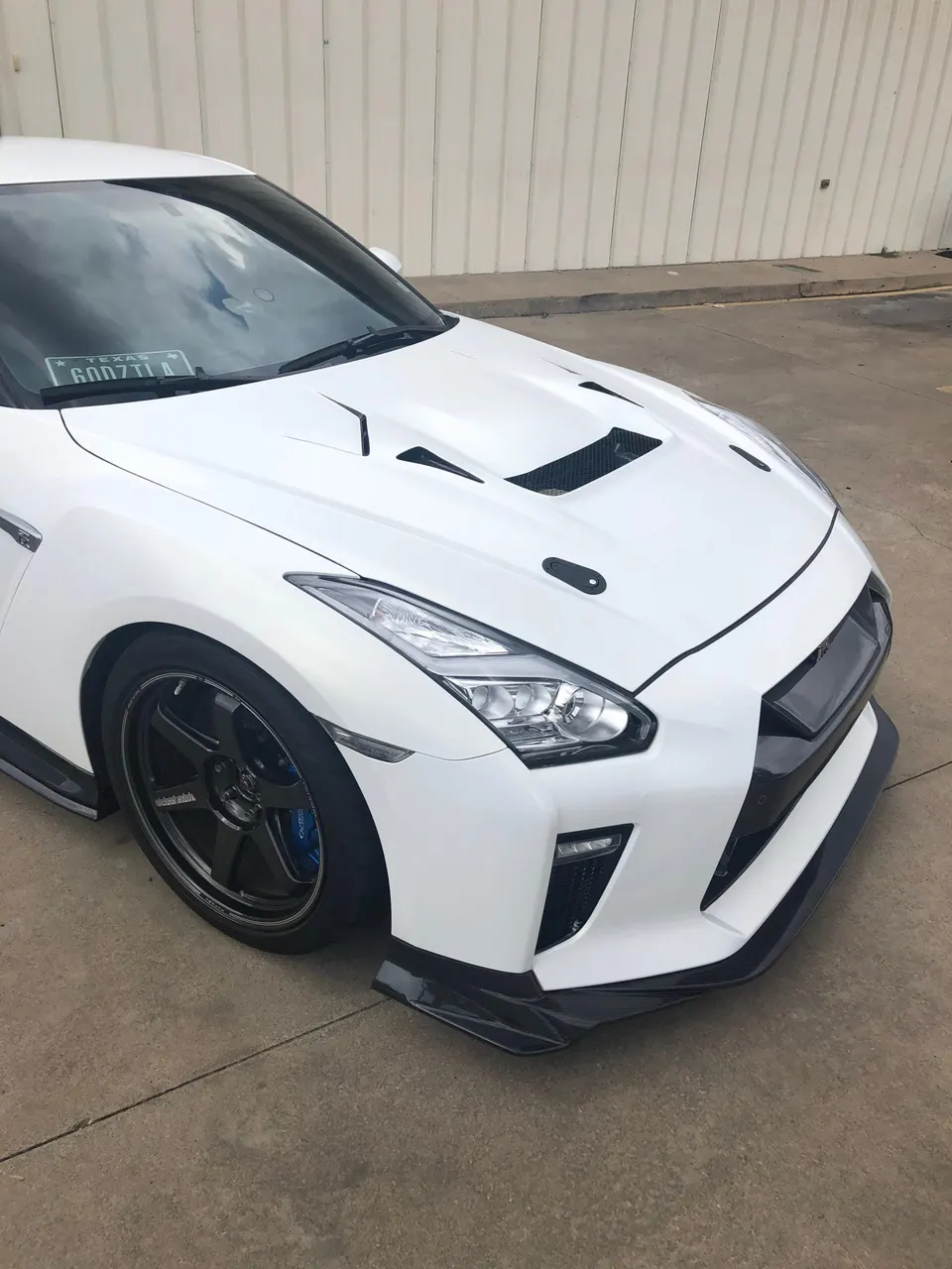 White Nissan GT-R R35 with custom vented hood, front splitter, and aftermarket wheels parked outdoors.