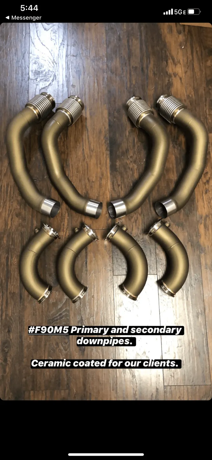 Ceramic coated primary and secondary downpipes for a BMW F90 M5 laid out on a wooden floor.