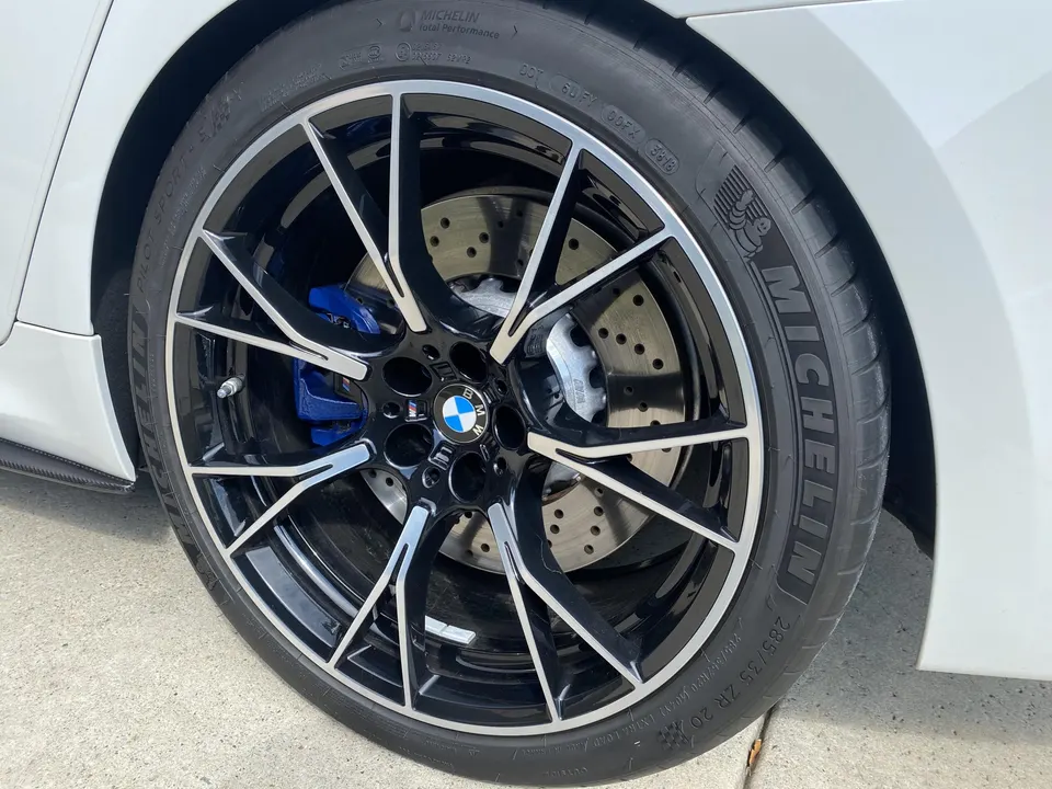 Close-up of a white BMW M car's black multi-spoke wheel with Michelin tire and blue brake calipers.