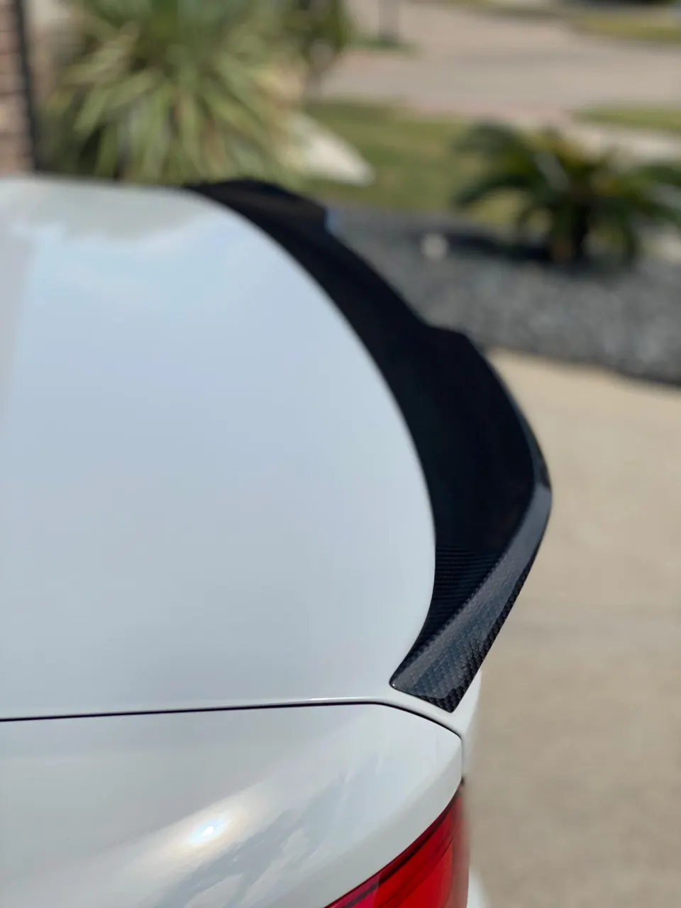 A close-up of a white car's rear with a carbon fiber spoiler.