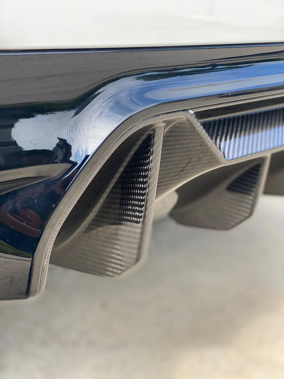 Close-up of a glossy carbon fiber rear diffuser on a performance car, showcasing its aerodynamic fins.