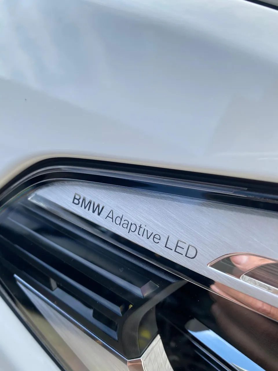 Close-up of a white BMW's Adaptive LED headlight, showcasing the detailed lighting technology.