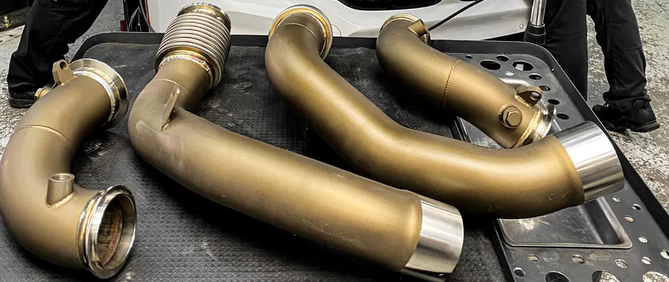Aftermarket exhaust downpipes and midpipes laid out on a tray in a performance tuning shop.