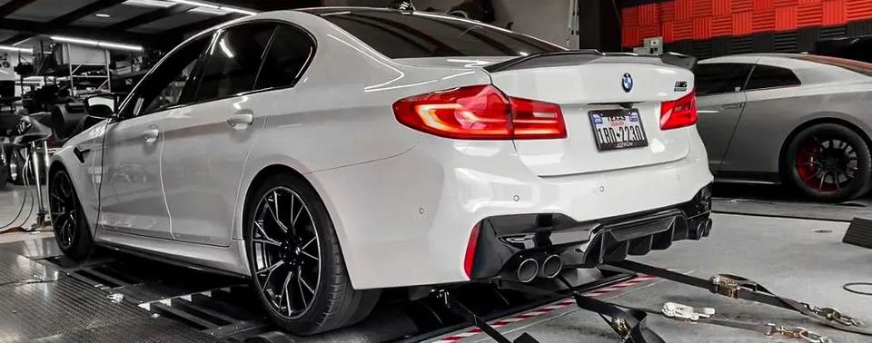 White BMW M5 on a dyno at a performance shop, showcasing its aftermarket exhaust and rear diffuser.