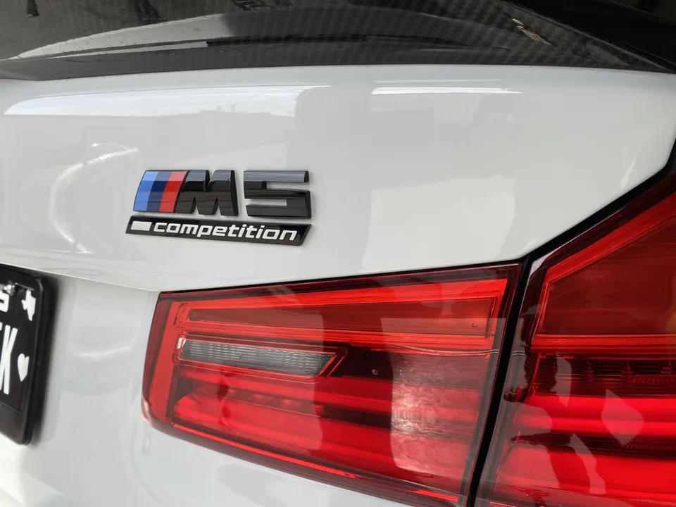 Close-up of a white BMW M5 Competition's rear trunk, featuring the M5 Competition badge and a red taillight.