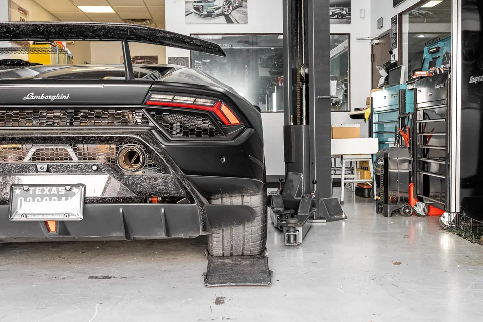 Rear view of a black Lamborghini Huracan with a large carbon fiber wing and aftermarket exhaust in a performance shop.