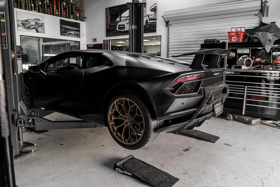 Matte black Lamborghini Huracan on a lift in a performance tuning shop, showcasing its carbon fiber wing and aftermarket wheels.