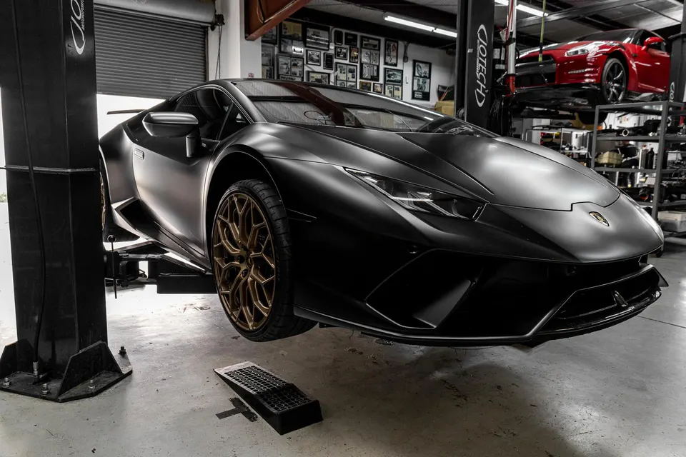 Matte black Lamborghini Huracan on a lift in the Jotech Motorsports shop with gold wheels.