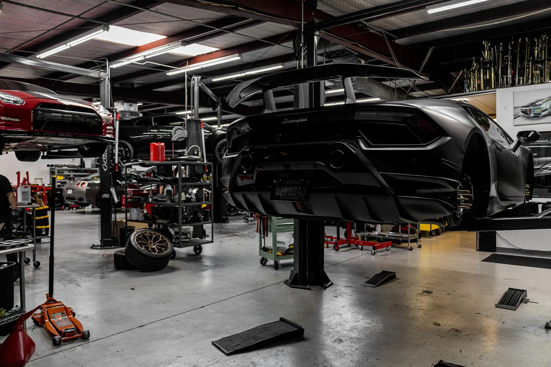 Black Lamborghini Huracan and red Nissan GT-R on lifts in a performance tuning shop garage.