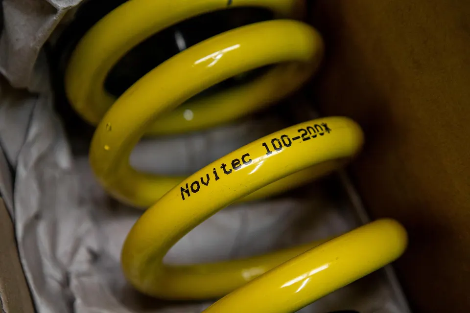 Close-up of a yellow Novitec suspension spring with 'Novitec 100-200x' text, still in its packaging.