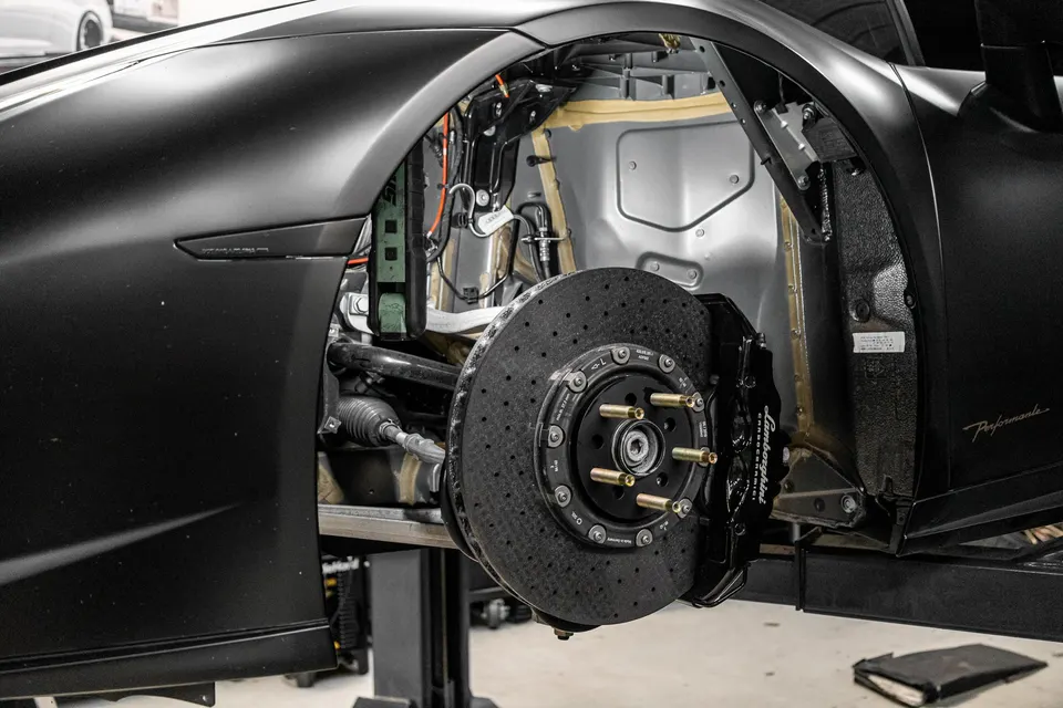 A Lamborghini Huracan Performante on a lift in a shop, with the front wheel removed, showcasing the carbon ceramic brakes and suspension components.