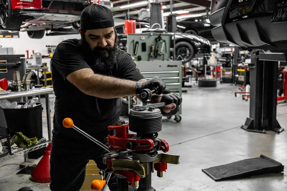 A mechanic in a performance shop uses a spring compressor to work on a coilover suspension component.