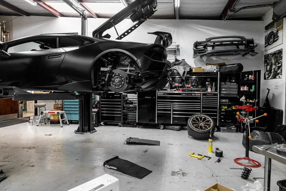 A matte black Lamborghini Huracan on a lift in a performance tuning shop, with its rear wheel removed exposing the brakes.