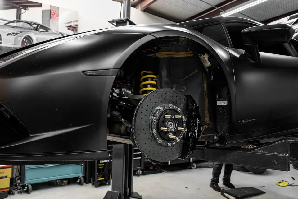 A matte black Lamborghini Huracan Performante on a lift in a shop, showcasing its carbon ceramic brakes and coilovers.