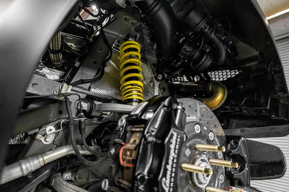 A close-up view of a Lamborghini's yellow coilover suspension and black brake caliper with a drilled rotor.