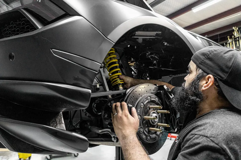 Mechanic installing a yellow coilover suspension and working on the brakes of a Lamborghini in a performance shop.