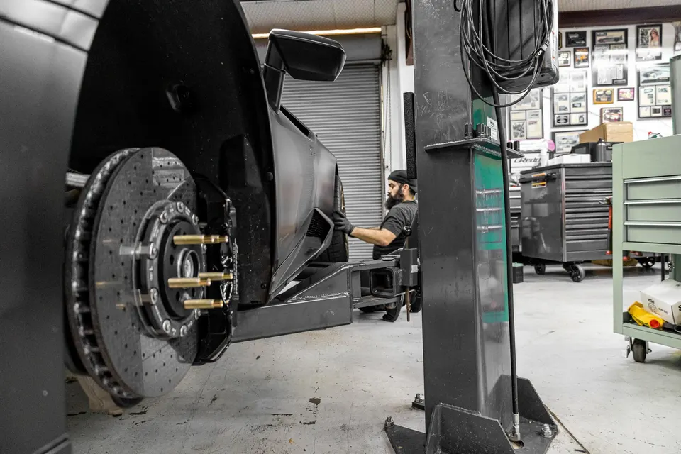 A Lamborghini Huracan on a lift in a performance shop, with a mechanic working on its carbon ceramic brakes.