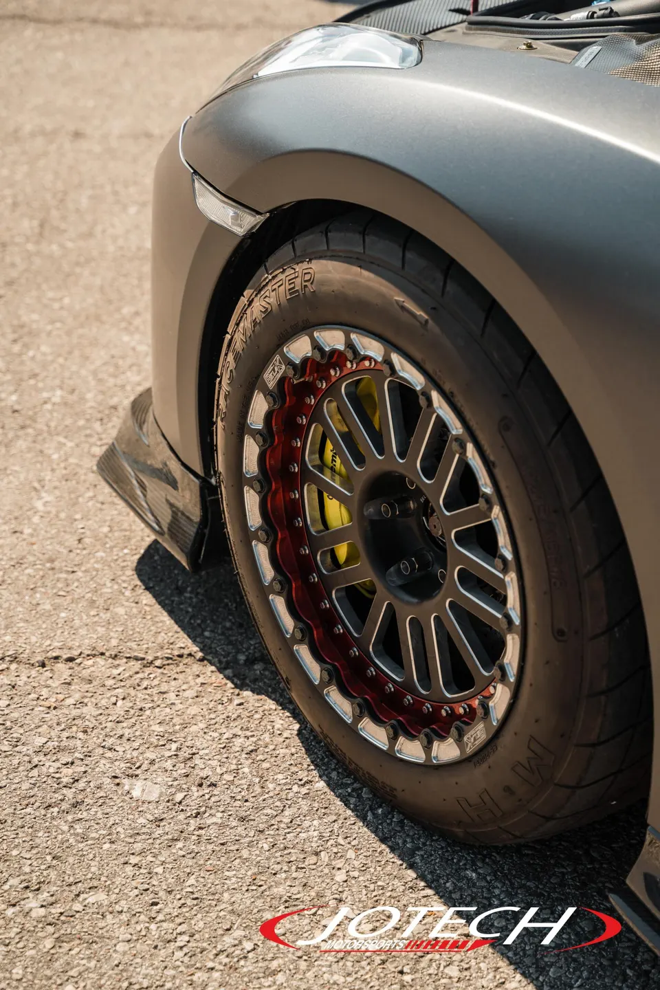 Close-up of a matte grey Nissan GT-R's front wheel with custom beadlock wheels, drag tires, and yellow brake calipers.