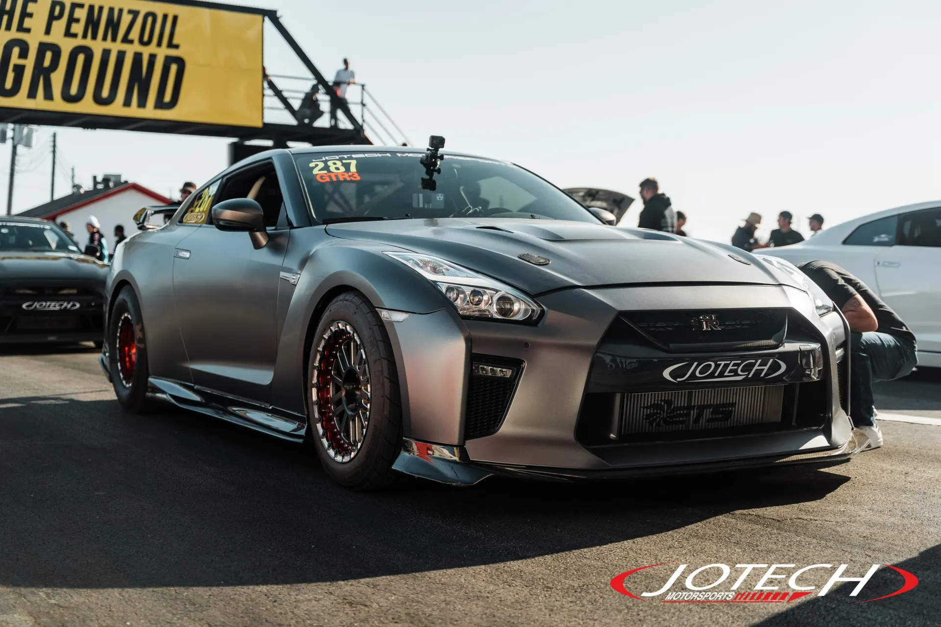 Matte grey Nissan GT-R R35 with aftermarket wheels and a large intercooler in the staging lane at a drag strip.