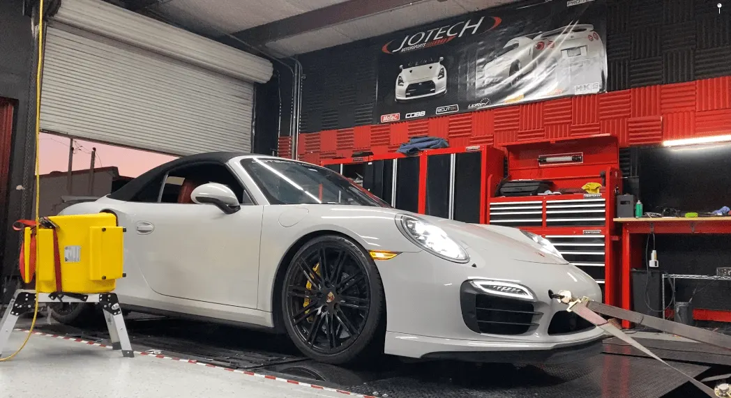 A white Porsche 911 convertible strapped to a dyno at Jotech Motorsports for performance tuning.