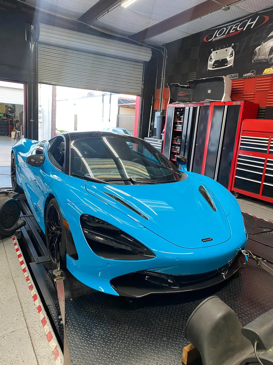 A vibrant blue McLaren 720S supercar strapped down on a dynamometer at Jotech Motorsports for performance tuning.