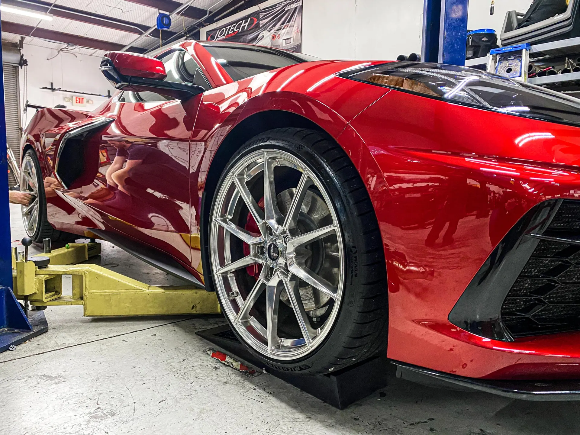 A red Corvette C8 on a lift in a performance shop, showcasing aftermarket wheels and tires.