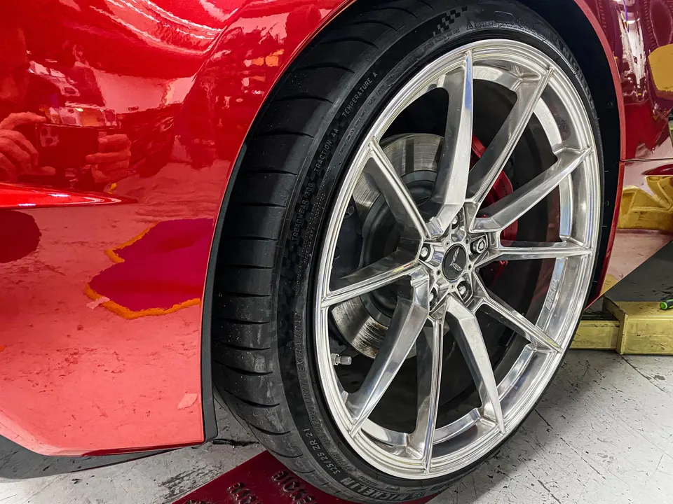 A close-up of a red Corvette's custom silver multi-spoke wheel with Michelin tires and red brake calipers in a shop.