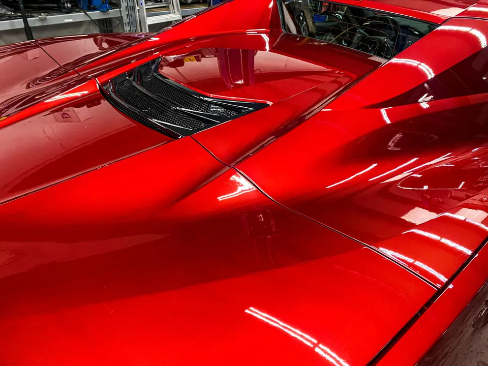 A close-up of the glossy red paint and rear deck of a Chevrolet Corvette C8, highlighting its sleek design.