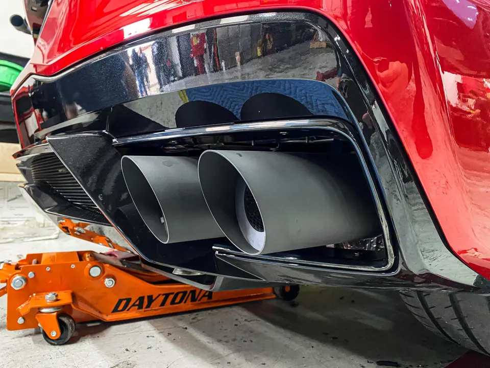 Close-up of a red car's aftermarket exhaust tips and rear diffuser in a shop, lifted by a Daytona jack.