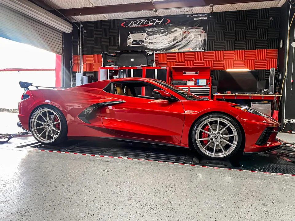A red Chevrolet Corvette C8 on a dyno at Jotech Motorsports performance tuning shop, ready for performance testing.