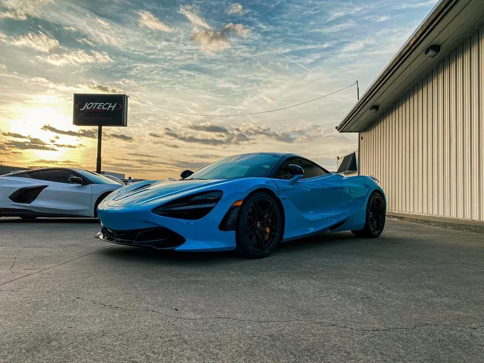 A blue McLaren 720S and a white C8 Corvette parked outside Jotech Motorsports at sunset