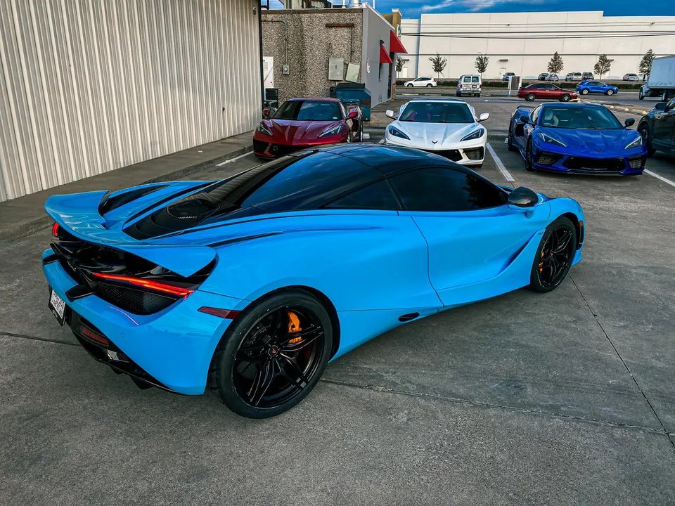 A blue McLaren 720S parked in a lot with a white Corvette C8 and a blue Corvette C8.