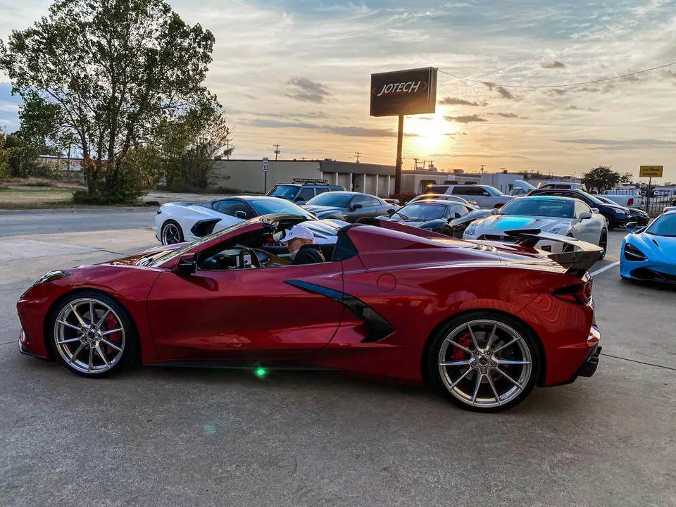 Red Chevrolet Corvette C8 convertible with aftermarket wheels parked at Jotech Motorsports during sunset.
