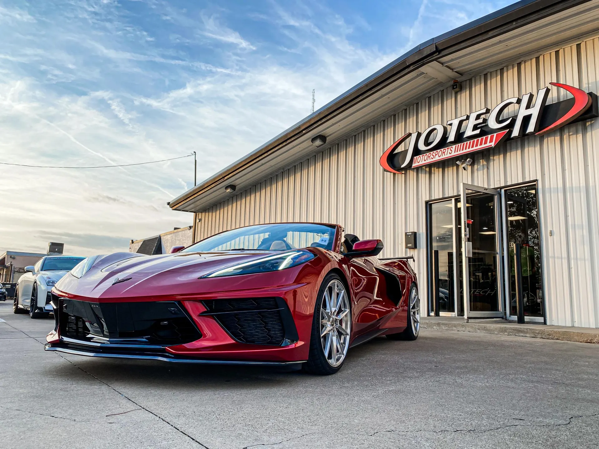 Red Chevrolet Corvette C8 with aftermarket wheels and a front splitter parked outside Jotech Motorsports performance shop.
