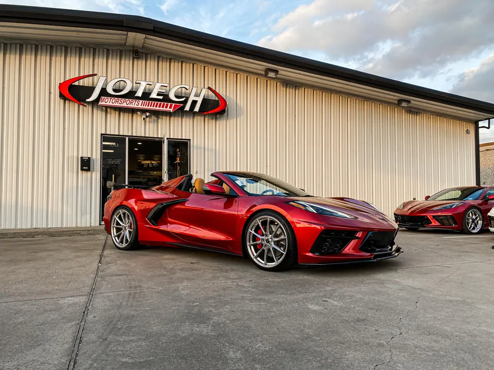 Two red C8 Corvettes with custom wheels parked outside Jotech Motorsports performance shop.