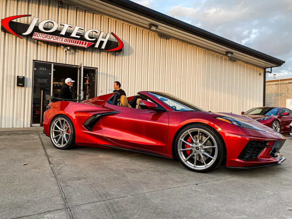 Red C8 Corvette convertible with custom wheels parked outside Jotech Motorsports performance tuning shop.