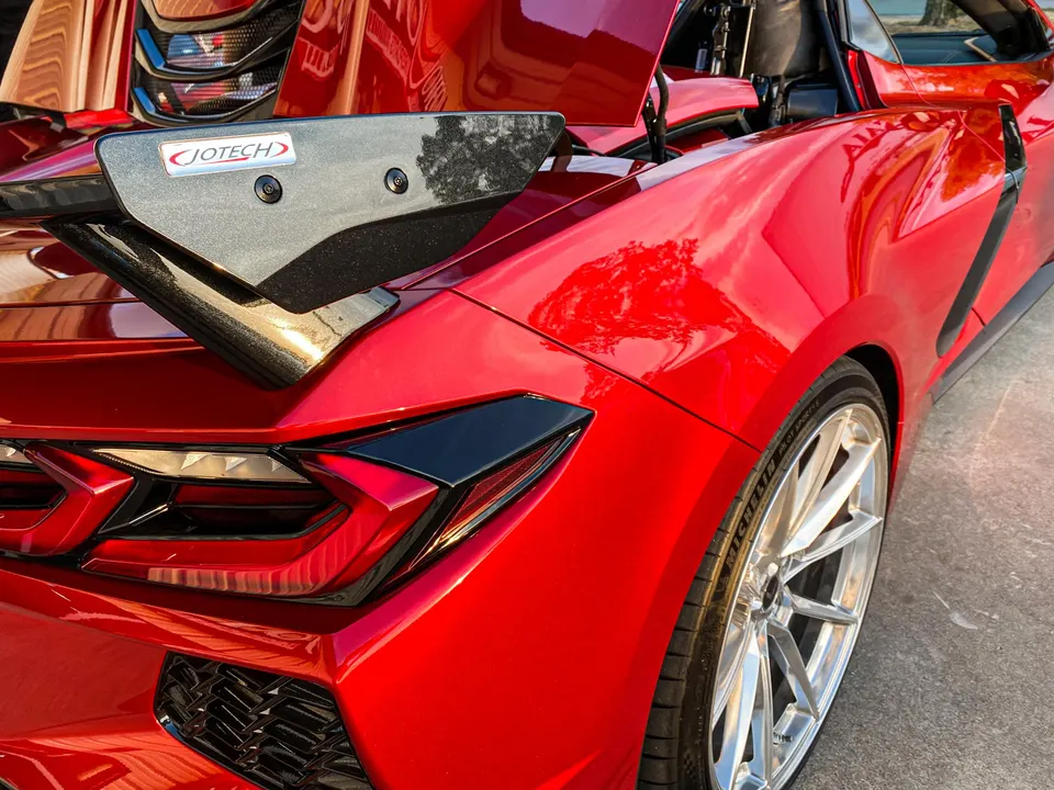 A red C8 Corvette with a Jotech carbon fiber wing and custom wheels, showcasing the rear quarter panel.
