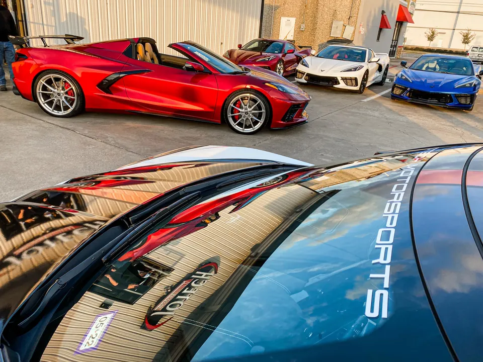 Multiple Chevrolet C8 Corvettes, including red, white, and blue models, gathered at an outdoor event.