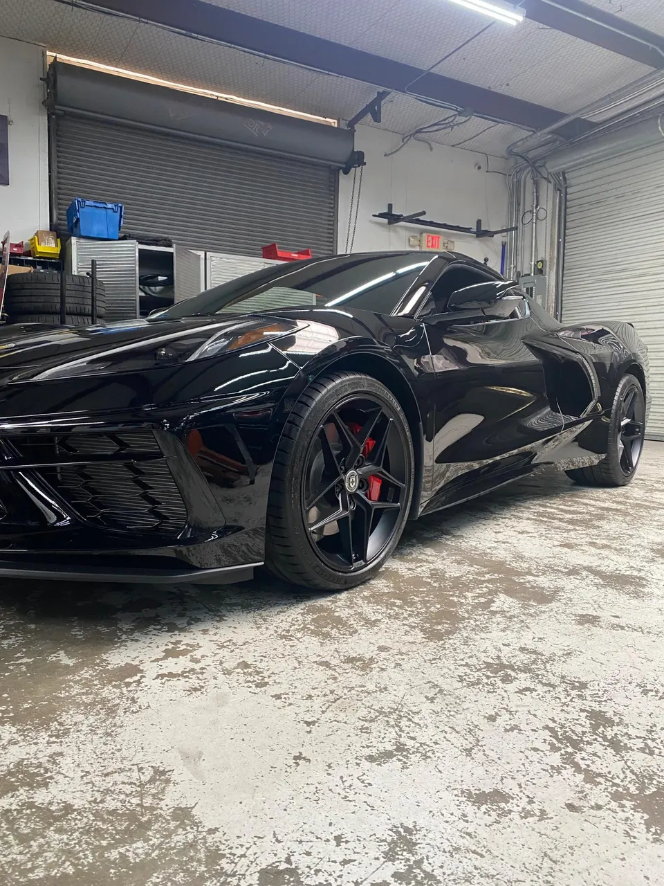 Black Chevrolet Corvette C8 with HRE wheels and red brake calipers parked inside a garage.