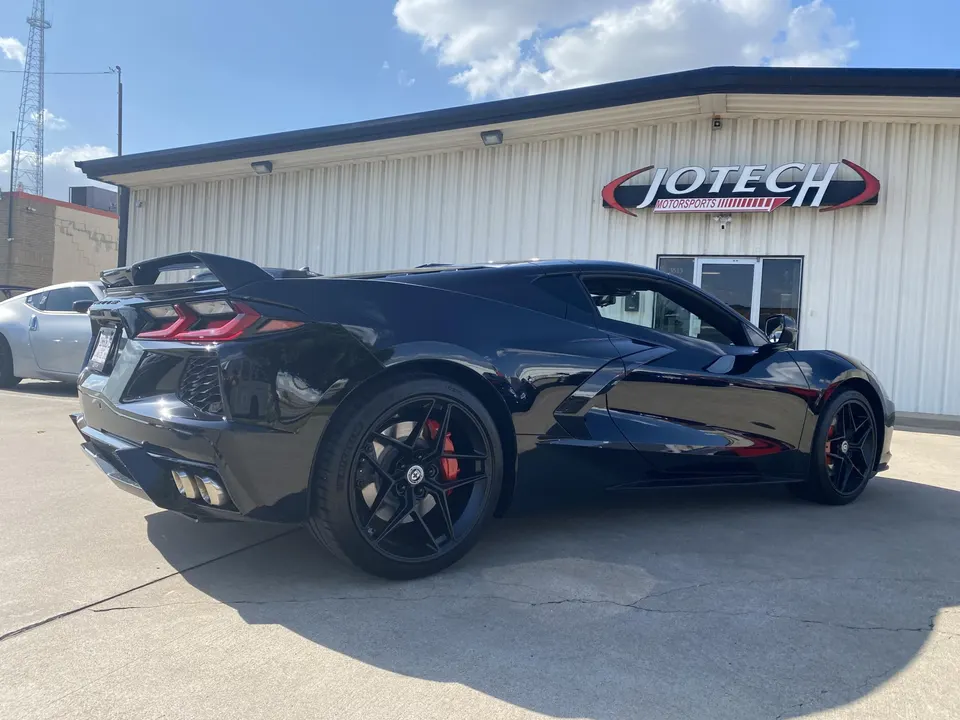 Black Corvette C8 with aftermarket wheels and rear wing parked outside Jotech Motorsports performance shop.